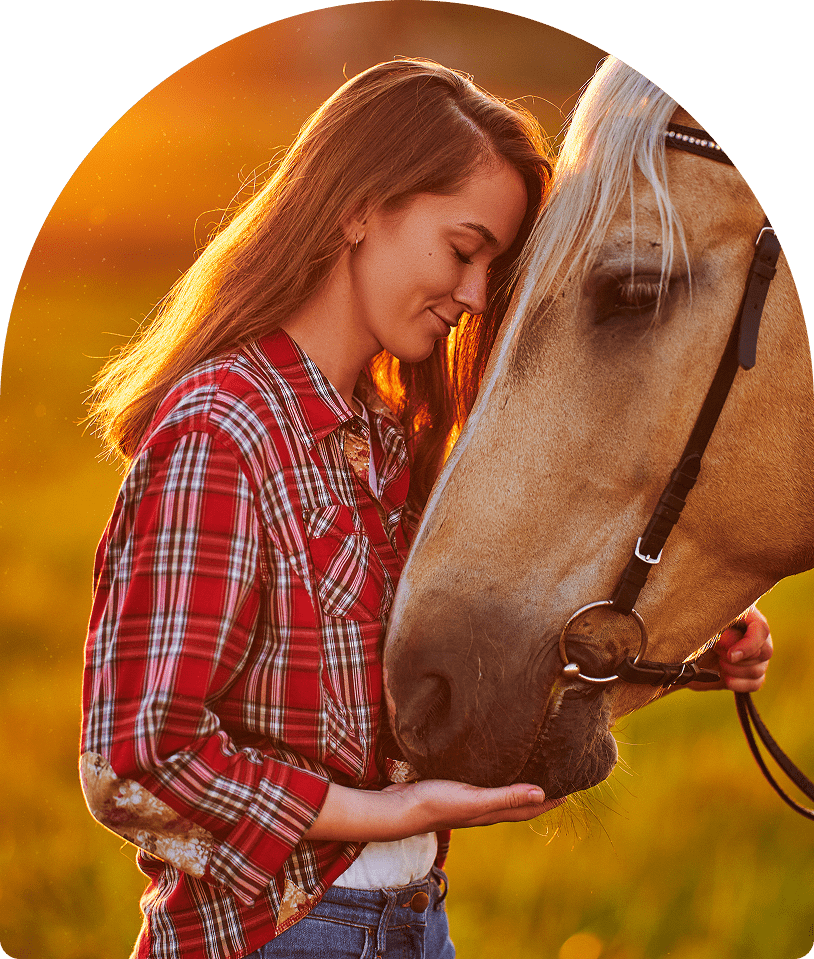 Woman in plaid shirt petting horse at sunset
