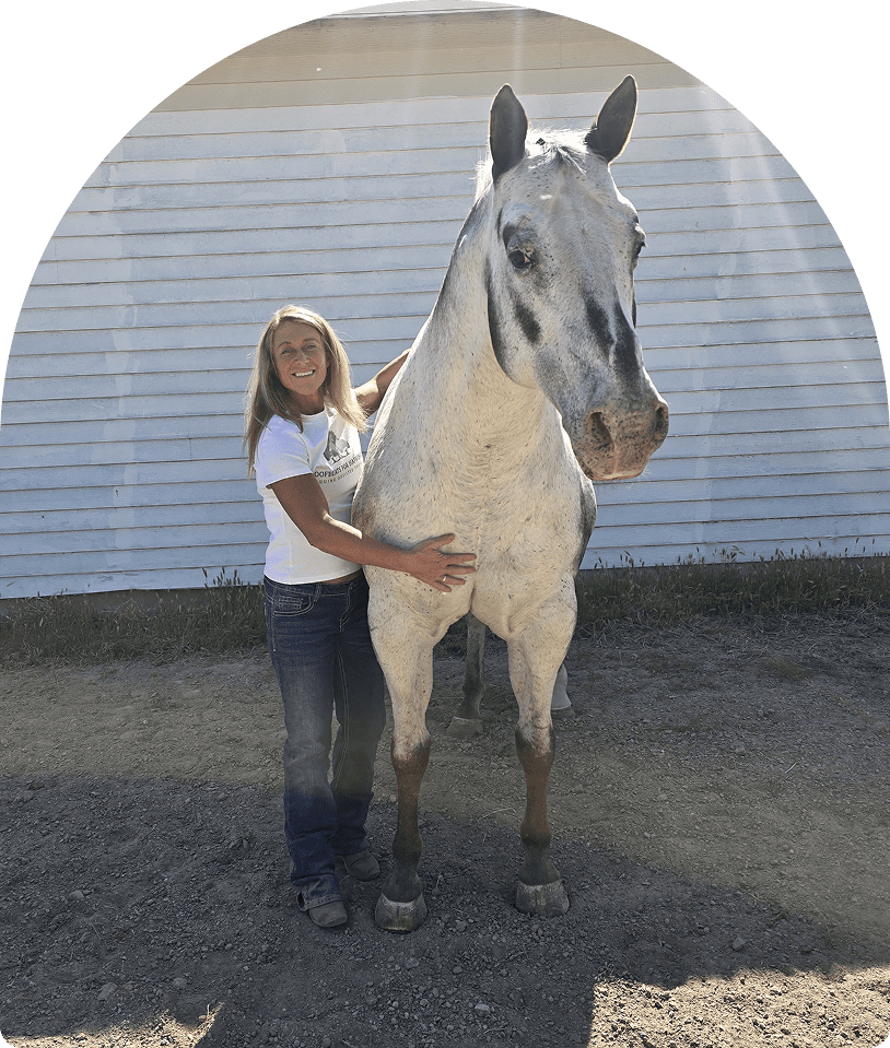 Smiling woman hugging gray horse by white barn